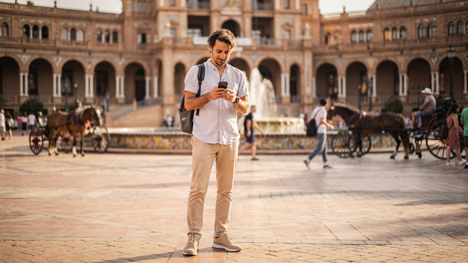 Un viajero consulta su teléfono, confirmando la conexión a internet en una plaza bulliciosa de Sevilla, España, durante la tarde.