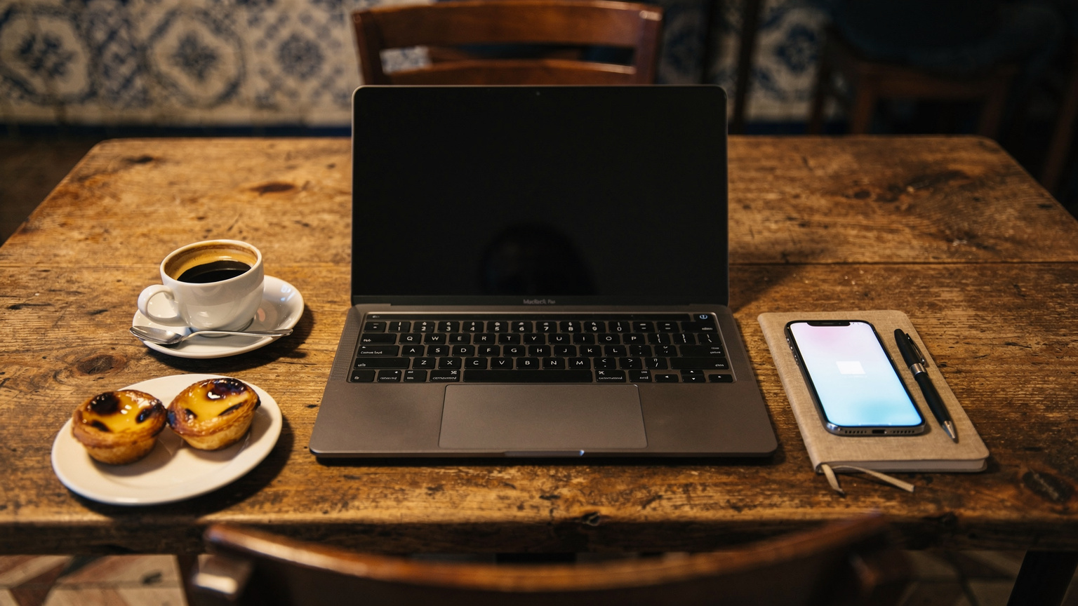 Uma mesa de café em Lisboa com um notebook aberto, um smartphone com um eSIM ativo, um copo de café e alguns pastéis de nata, sugerindo um ambiente de trabalho remoto e conectividade.