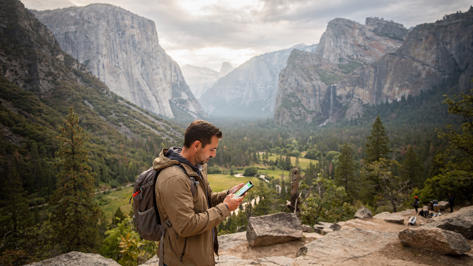 Zamyšlený cestovatel se dívá na obrazovku svého telefonu s mapou, obklopený majestátními žulovými útesy a borovicemi v Yosemitském národním parku, hledá signál.