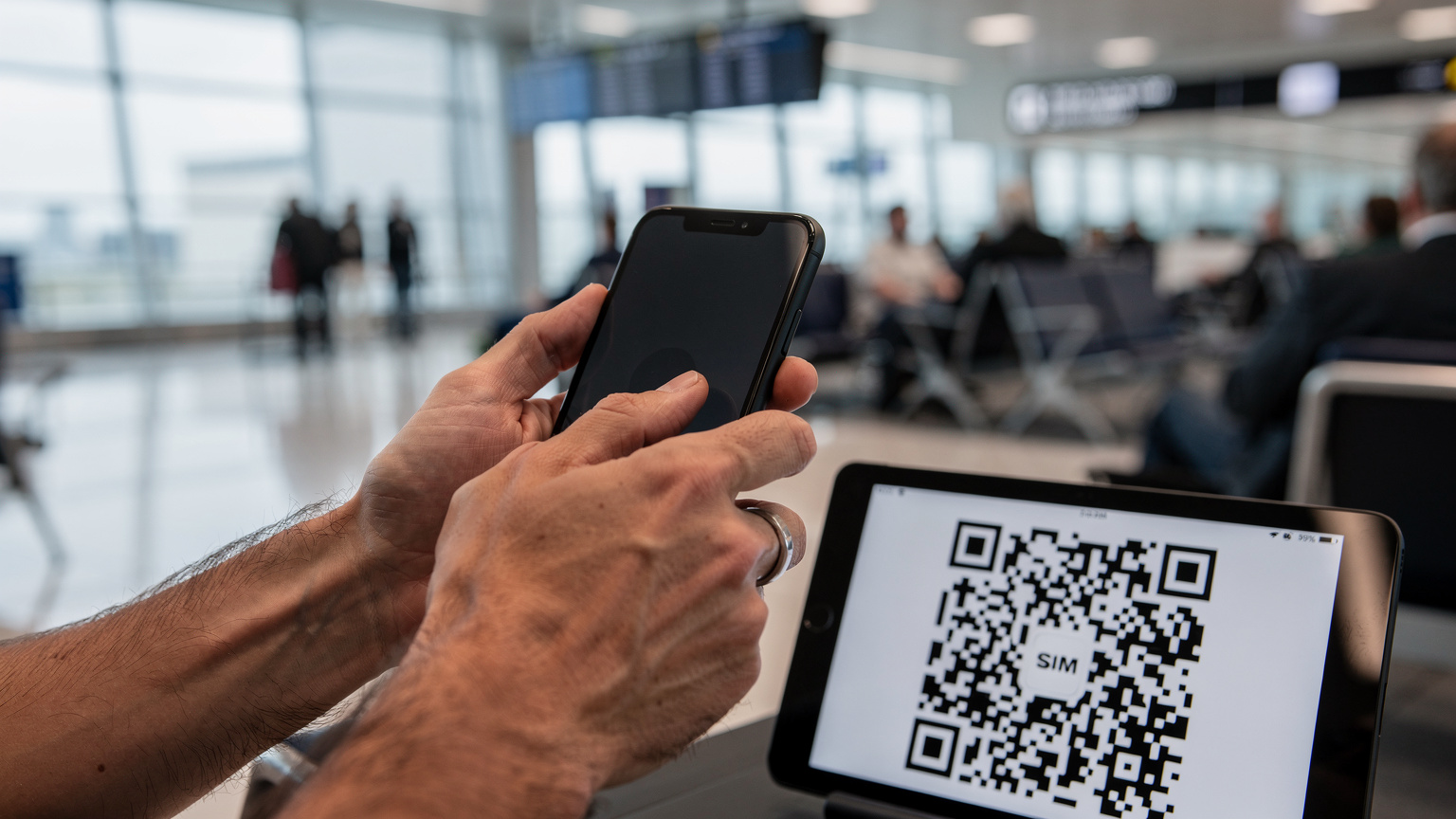 Manos de un viajero escaneando un código QR desde otro dispositivo para activar una eSIM en su móvil, con el fondo desenfocado de una sala de espera en el aeropuerto de Heathrow.
