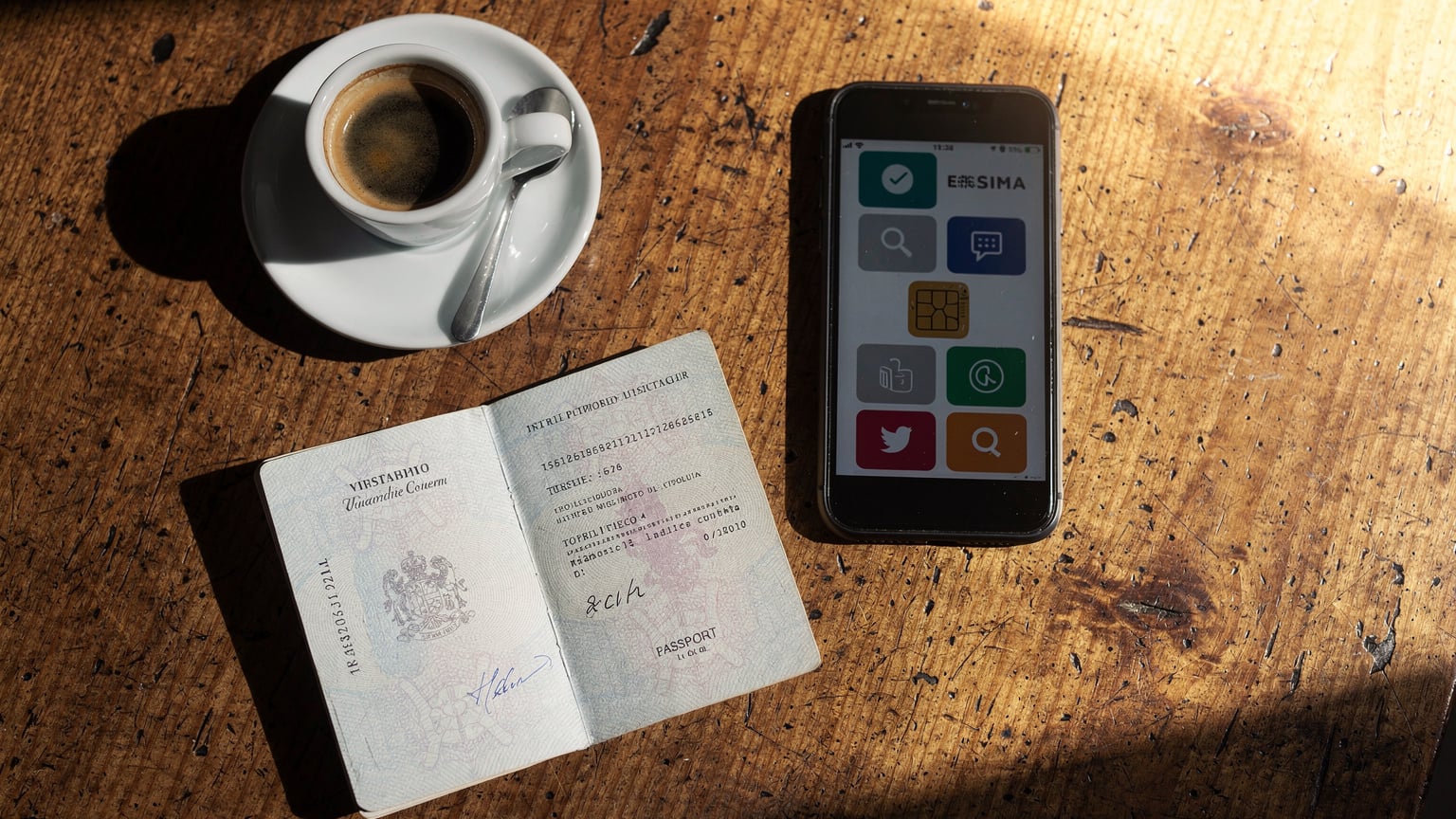 A close-up of a traveler's passport, a smartphone showing an activated eSIM profile, and a small cup of espresso on a wooden cafe table in Italy.