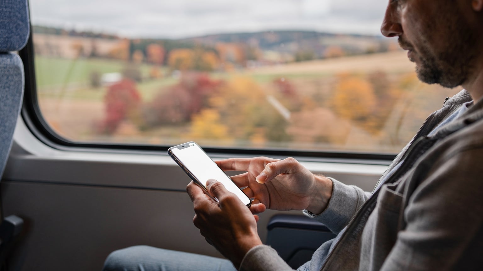 A traveler activates an eSIM on their smartphone while seated on a high-speed train, autumnal European countryside visible through the window.