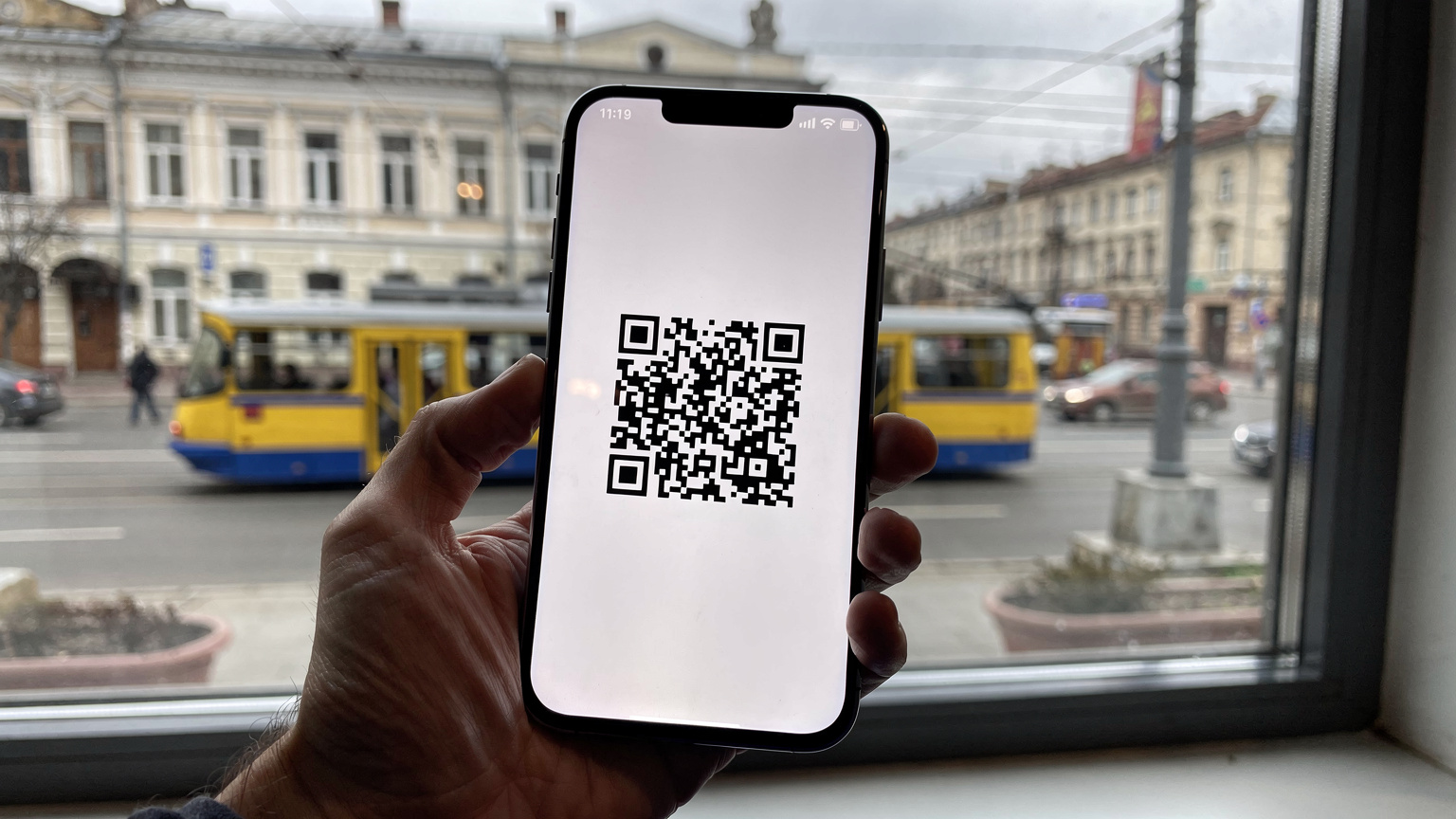 Сучасний смартфон з QR-кодом для активації eSIM на екрані, на фоні вікна, що виходить на міську вулицю Києва.