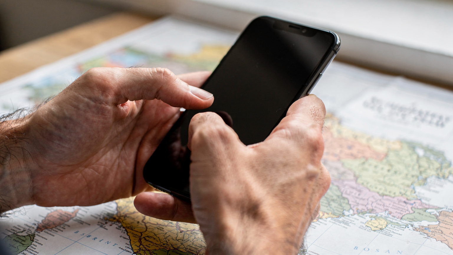 Detailní záběr rukou cestovatele, který v telefonu kontroluje nastavení APN pro svou eSIM, zatímco v pozadí je rozmazaná mapa Balkánu.