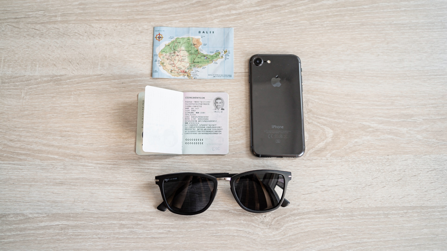 An overhead flat-lay shot featuring a passport, a smartphone with a Cellesim logo, a small map of Bali, and a pair of sunglasses, ready for travel.