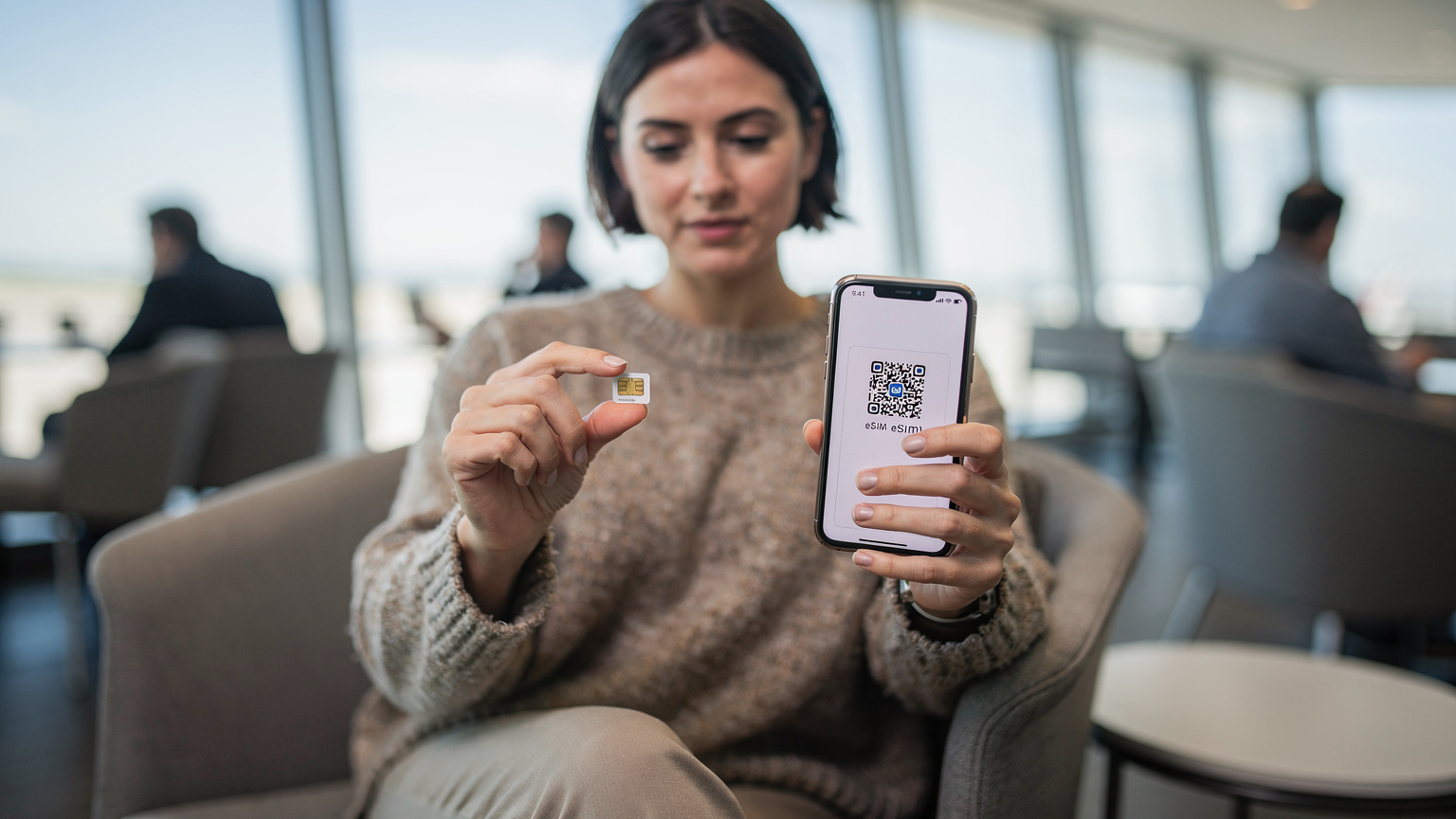 A female traveler in a brightly lit airport lounge is comparing a tiny physical SIM card held between her fingers to her smartphone screen which clearly displays an eSIM activation QR code, with a subtle look of contemplation.
