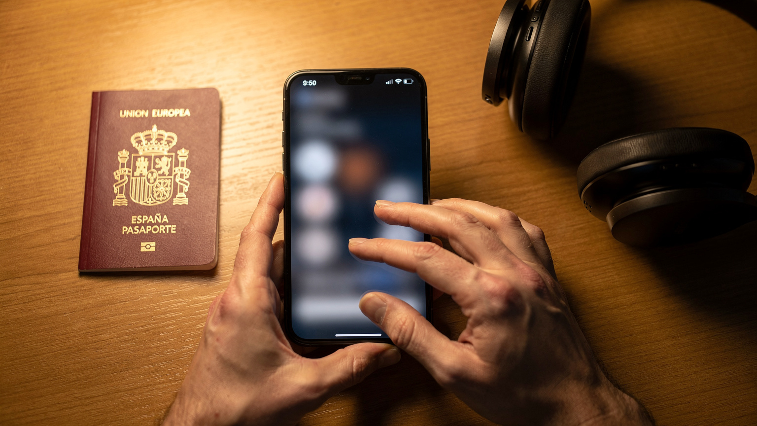 Primer plano de manos de un viajero ajustando la configuración de la eSIM en un smartphone, con un pasaporte español y auriculares de viaje en una mesa de madera.