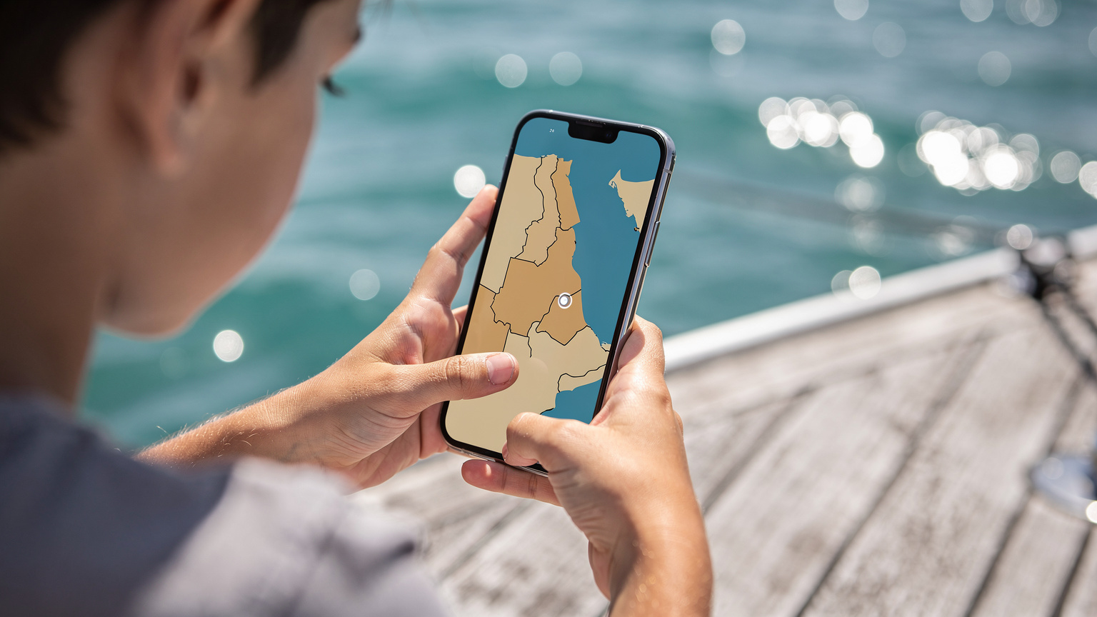A child's hand holding a smartphone displaying a map app with a pin dropped near Port Sudan on the Red Sea, while a parent's hand gently points to a feature on the screen.