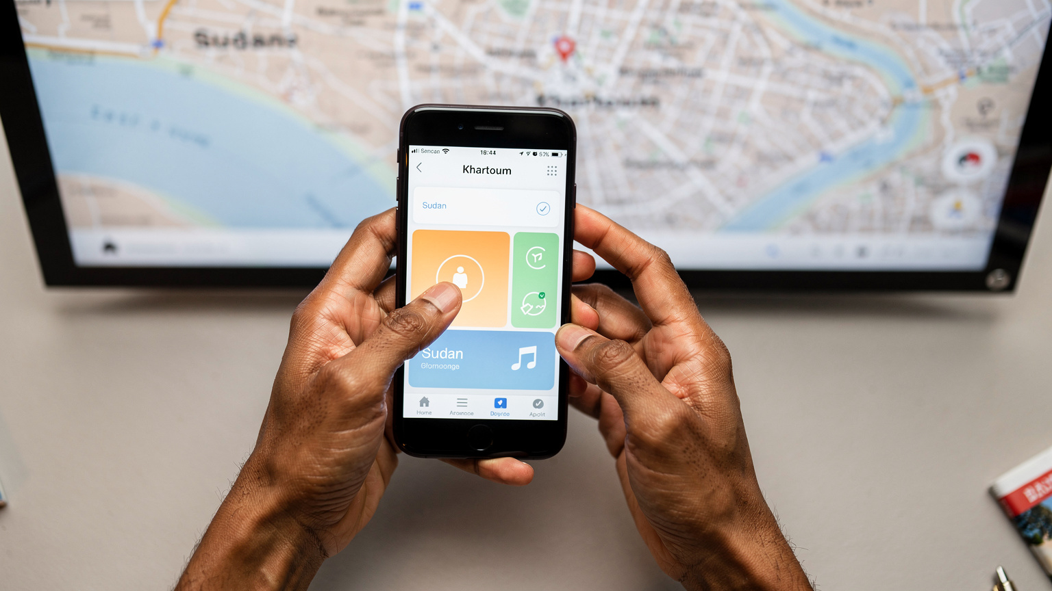 A person's hands delicately hold a smartphone, displaying the Cellesim app's activation screen for a Sudan eSIM, with a blurred map of Khartoum in the background.