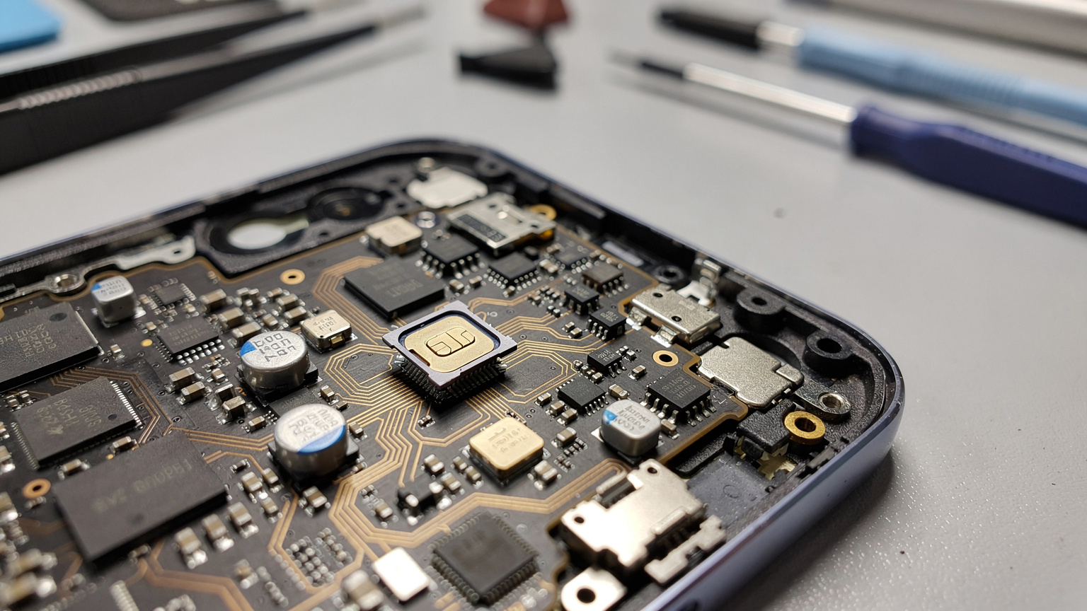 Nahaufnahme eines zerlegten Smartphones, das den kleinen, integrierten eSIM-Chip auf der Hauptplatine zeigt, umgeben von anderen Mikrokomponenten.