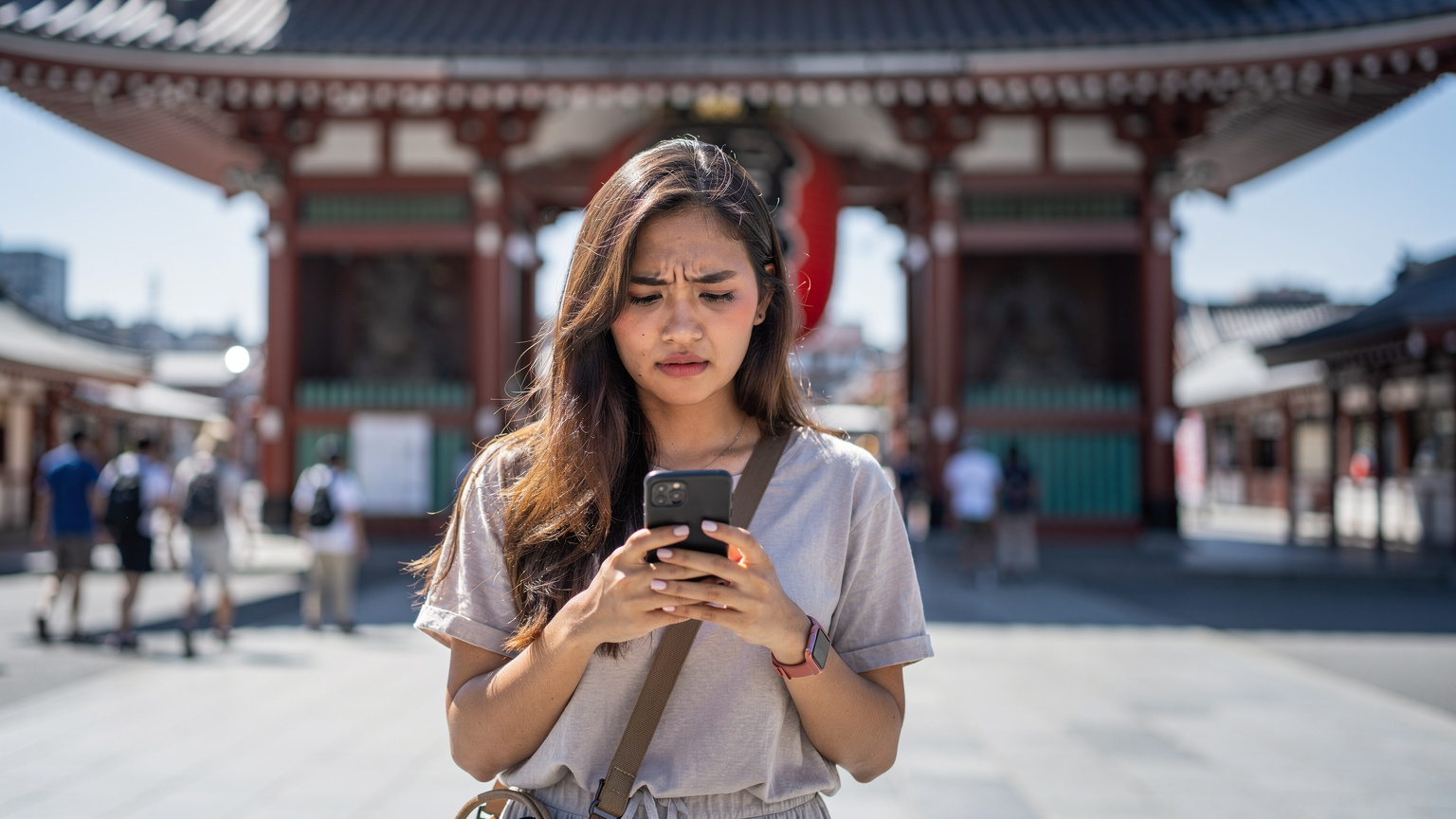 Seorang traveler wanita tampak sedikit frustasi memegang ponsel di depan Kuil Senso-ji, Tokyo, mungkin menghadapi masalah koneksi.
