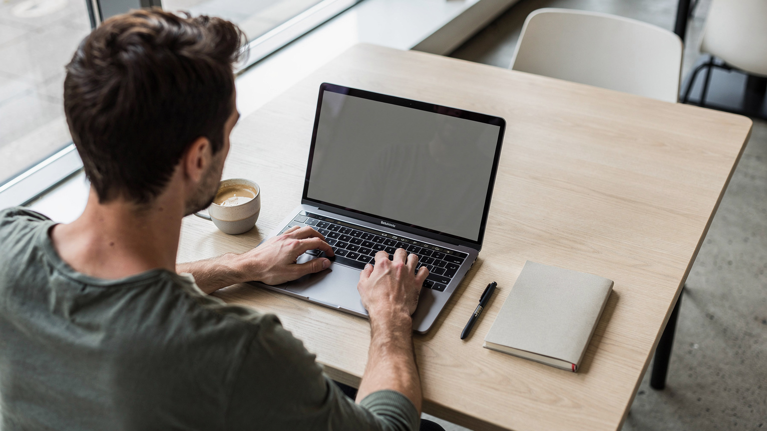 Een digital nomad werkt geconcentreerd op een laptop in een lichte, minimalistische co-working space in Berlijn, met een kop koffie en een notitieboekje ernaast.
