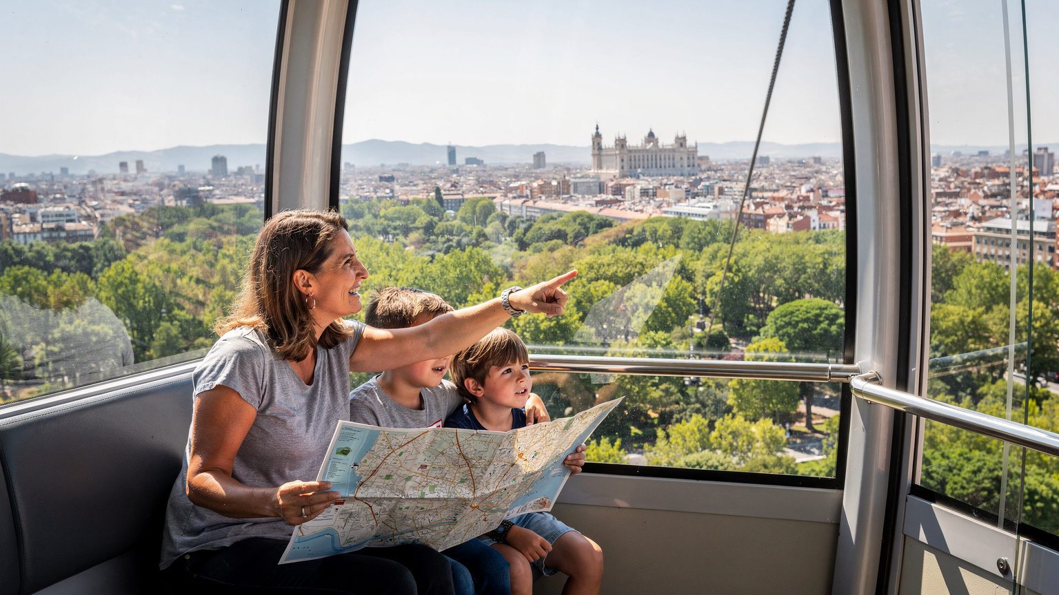 Madrid'deki bir teleferik kabininde, dışarıyı seyreden bir kadın ve iki çocuğu, kadının elinde açık bir harita var.