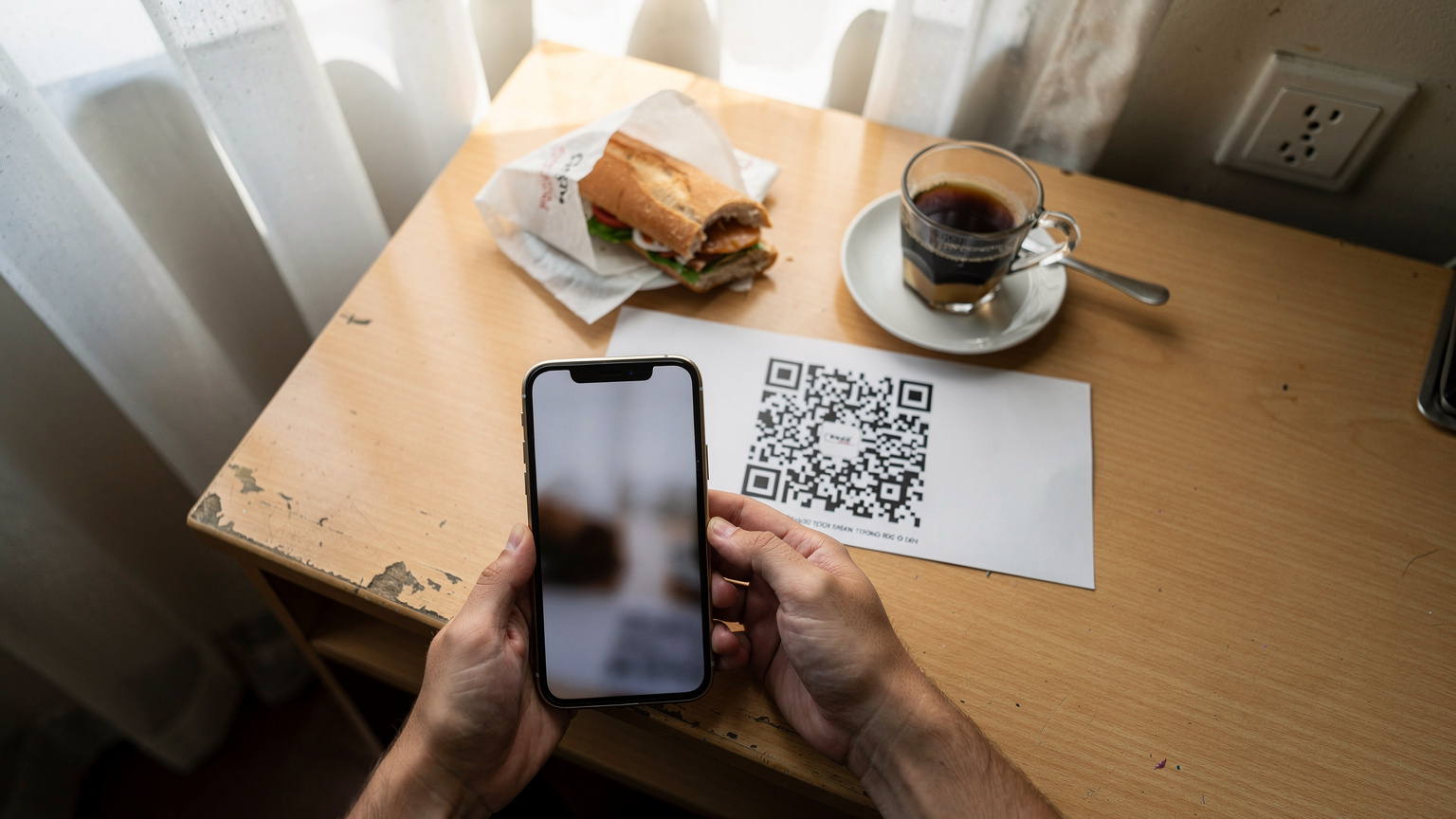 Un viaggiatore sta scansionando un QR code per attivare la sua eSIM, con la luce del mattino che filtra attraverso la finestra di una stanza d'albergo economica in Vietnam.