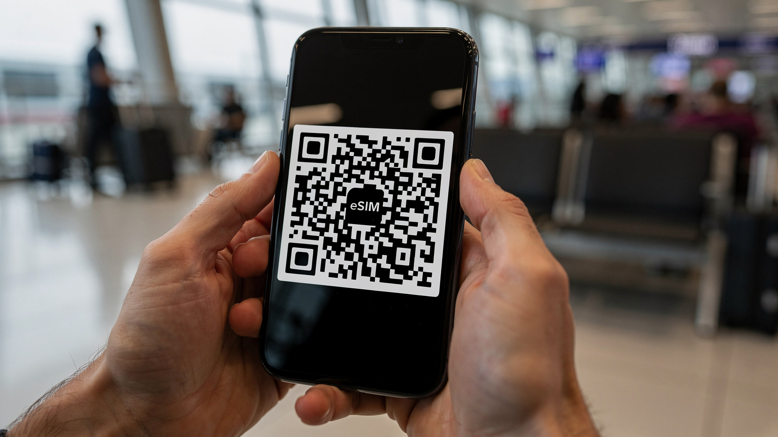Eine Nahaufnahme von Händen, die ein Smartphone halten, auf dem der QR-Code zur eSIM-Aktivierung angezeigt wird. Der Hintergrund ist leicht unscharf und zeigt eine geschäftige Reisestation, möglicherweise einen Flughafen oder Bahnhof.