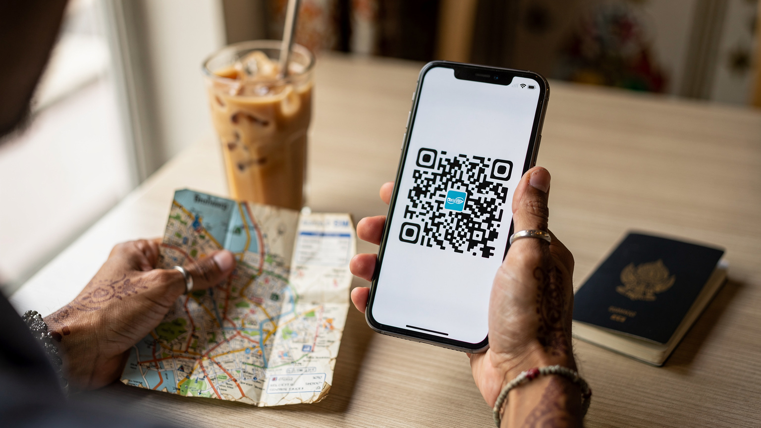 एक व्यक्ति अपने स्मार्टफोन पर QR कोड स्कैन करके eSIM एक्टिवेट कर रहा है, उसके हाथ में एक थाईलैंड टूरिस्ट मैप है।