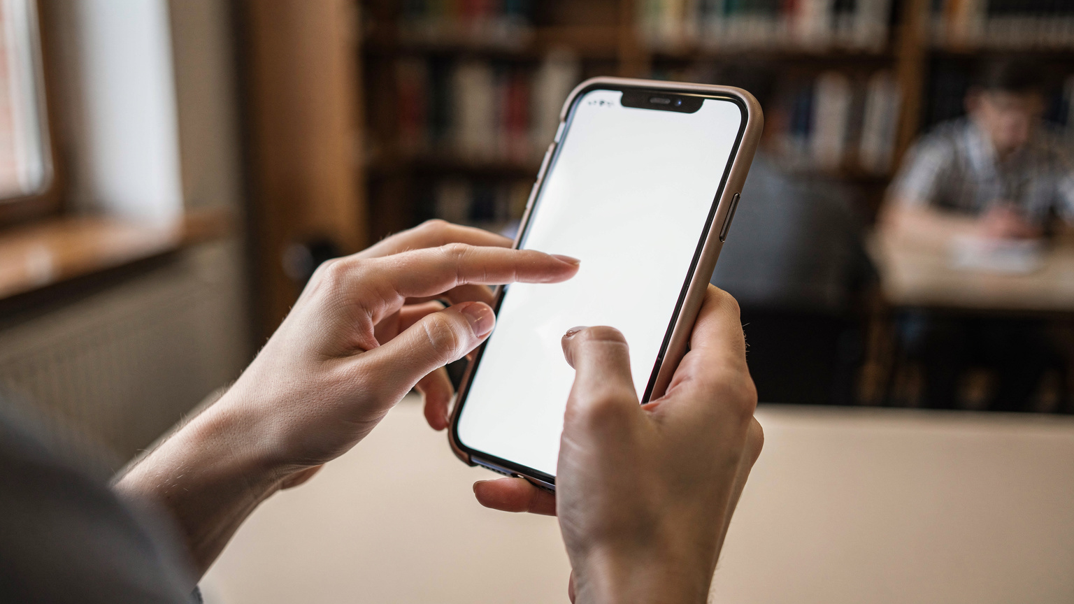 Крупний план рук студентки, яка налаштовує eSIM на своєму iPhone в університетській бібліотеці Кракова, Польща.