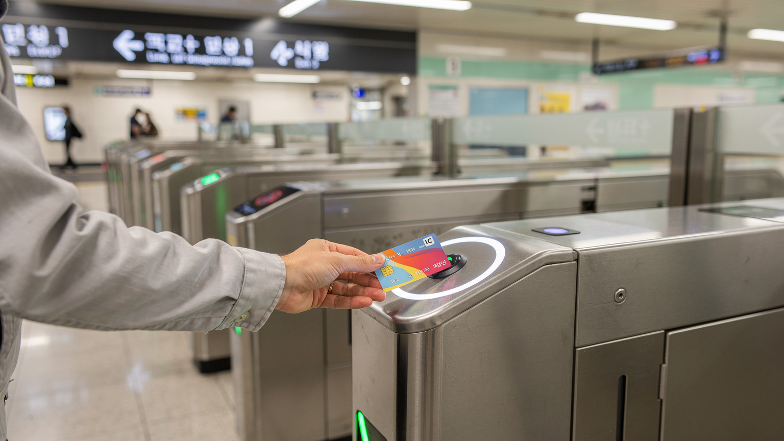 Sebuah tangan wisatawan sedang menyentuhkan kartu transportasi publik seperti T-Money atau Suica ke gerbang tiket kereta bawah tanah yang modern dan bersih di Seoul, Korea Selatan.