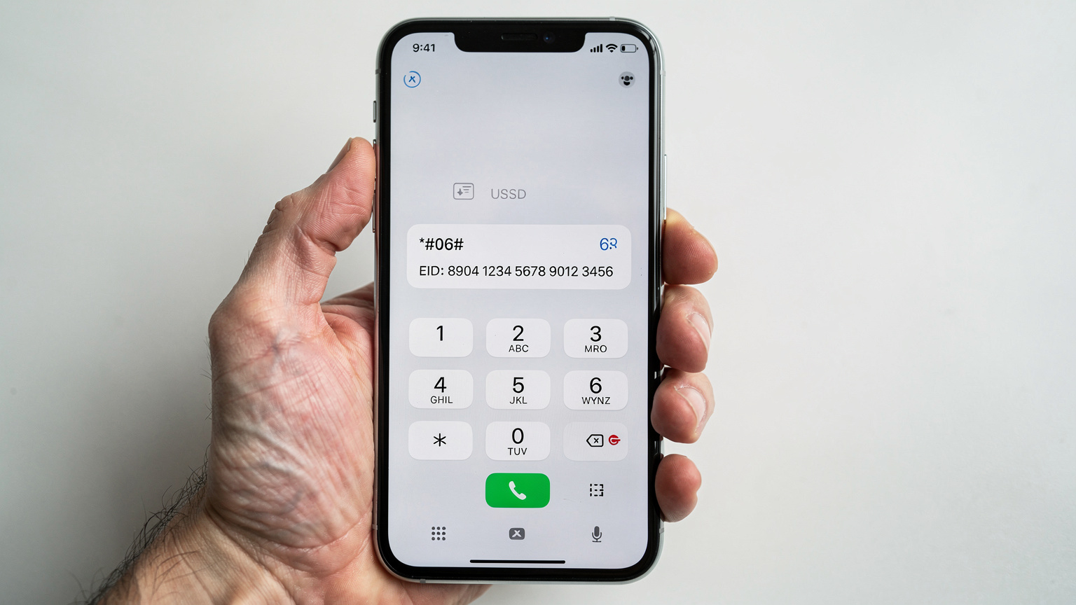 Eine Nahaufnahme eines Smartphones, das den USSD-Code *#06# auf dem Display anzeigt und darunter die EID-Nummer für die eSIM-Identifikation. Eine menschliche Hand hält das Telefon.