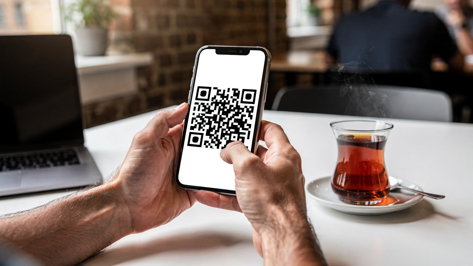 Bir dijital nomadın elinde akıllı telefon ve bir fincan çay ile bir QR kodu taradığı yakın çekim. Telefon ekranında bir eSIM kurulum arayüzü görülebilir, ancak ekrandaki metin okunaksızdır.