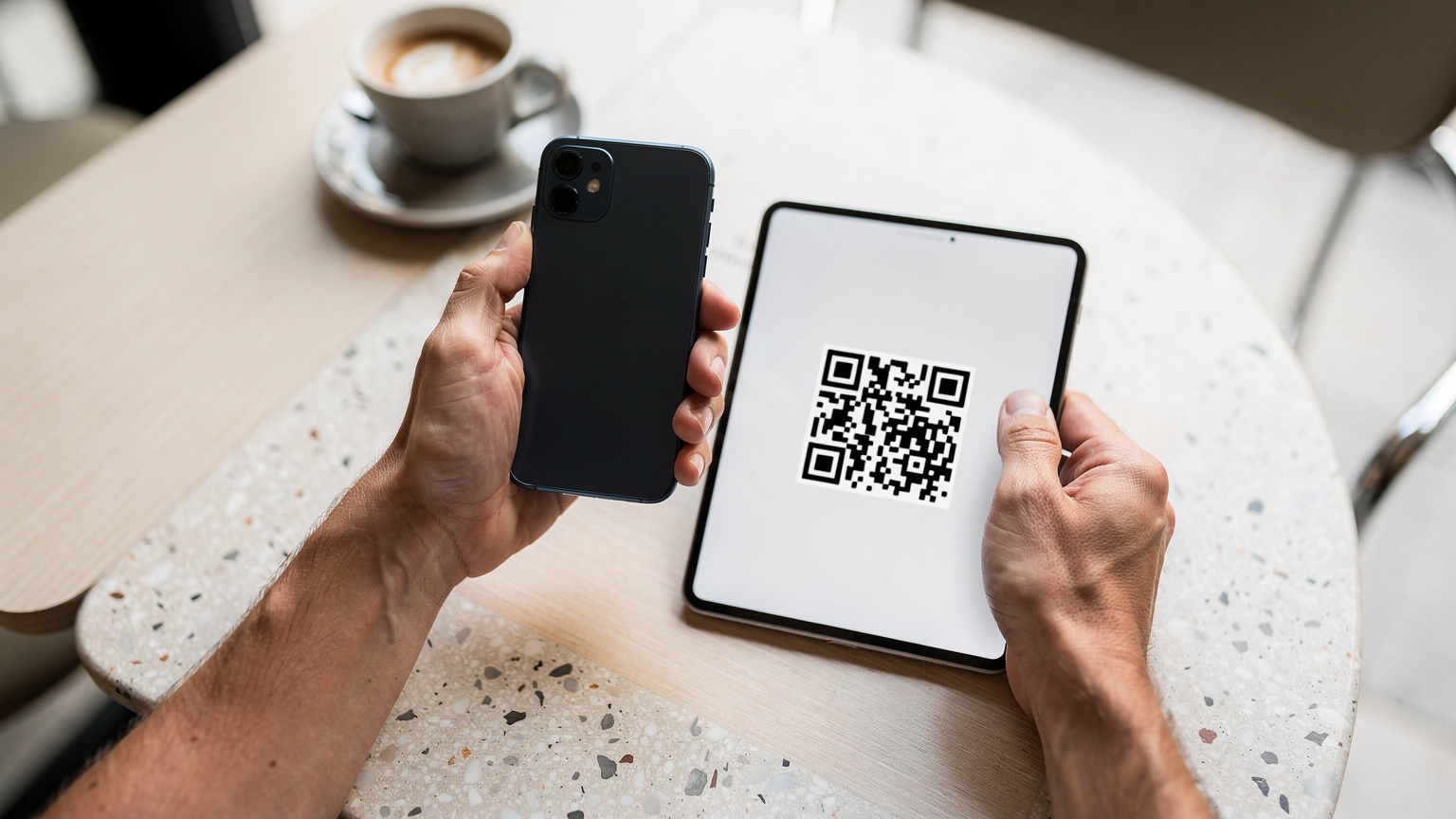 Un primo piano delle mani di una persona che tiene uno smartphone mentre scansiona un codice QR da un altro dispositivo o da una stampa, in un ambiente luminoso e moderno.