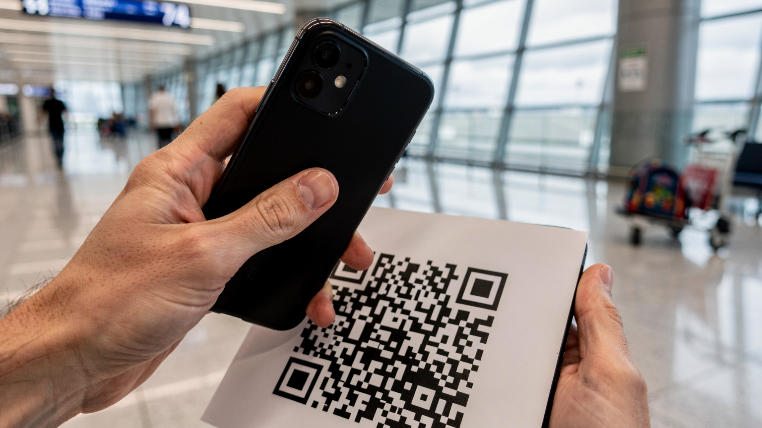 A parent quickly scans a QR code to activate an eSIM plan on their smartphone inside a brightly lit airport terminal, with luggage and children in the background.