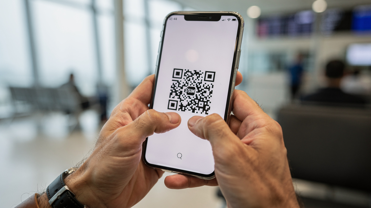 Close-up of a traveler's hands holding a smartphone, scanning a QR code for eSIM activation, with a blurred backdrop of an airport lounge.