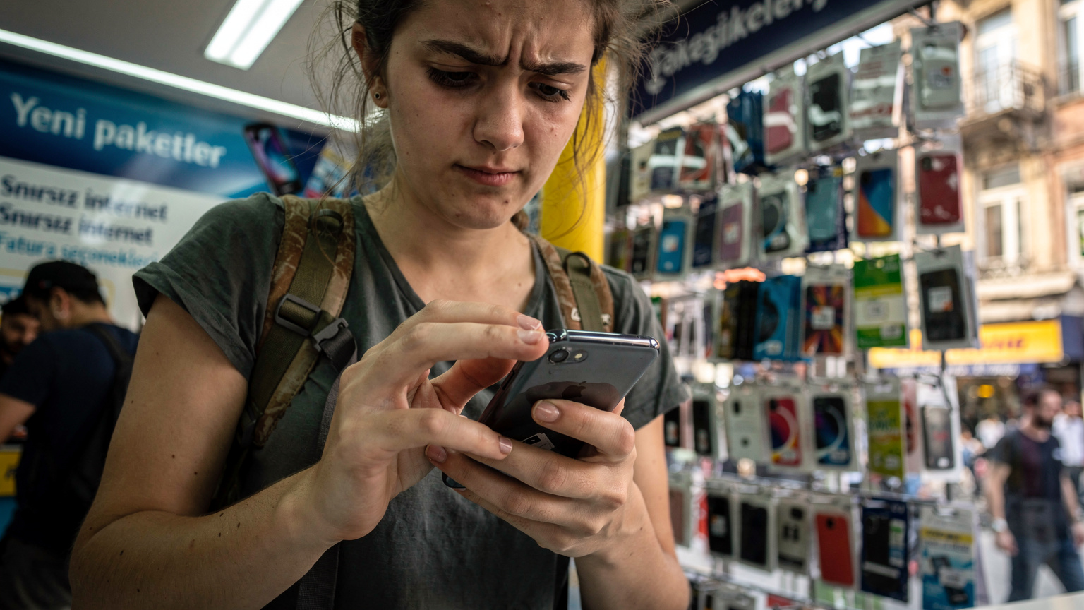 O turistă privește confuză meniul de pe un telefon, încercând să înțeleagă instrucțiunile în limba turcă pentru activarea unui SIM local într-un magazin aglomerat de telefonie mobilă din Istanbul.