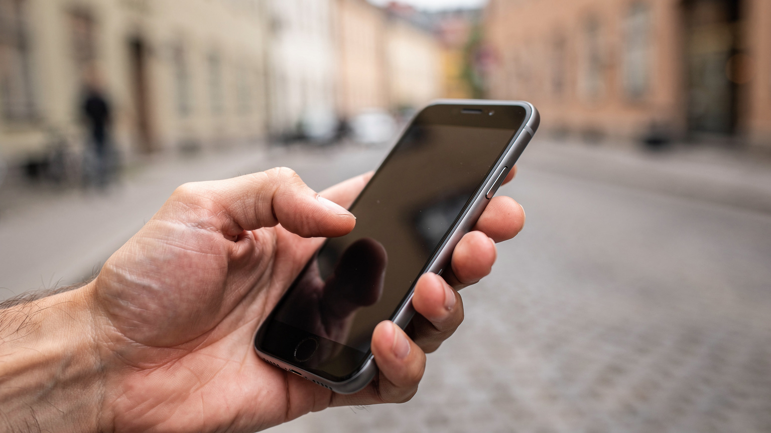 En nära bild av en hand som håller en smartphone med skärmen vänd mot betraktaren, där nätverksinställningarna är synliga med fokus på eSIM-profiler och APN-alternativ. Bakgrunden är en urban miljö i Stockholm.