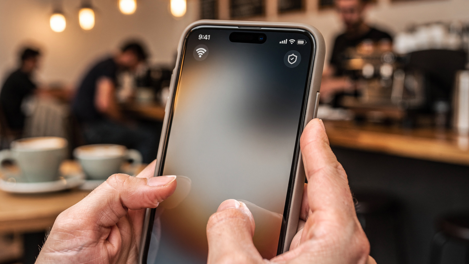 A close-up of a smartphone screen displaying a Wi-Fi symbol and a data-saving mode icon, with a blurred backdrop of a cozy cafe interior.