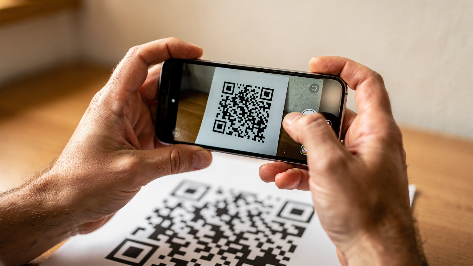 Szczegółowe zdjęcie dłoni osoby trzymającej smartfon, na którym widać proces skanowania kodu QR do aktywacji eSIM, z niewyraźnym tłem przedstawiającym wnętrze typowego niemieckiego domu lub kwatery pracowniczej.