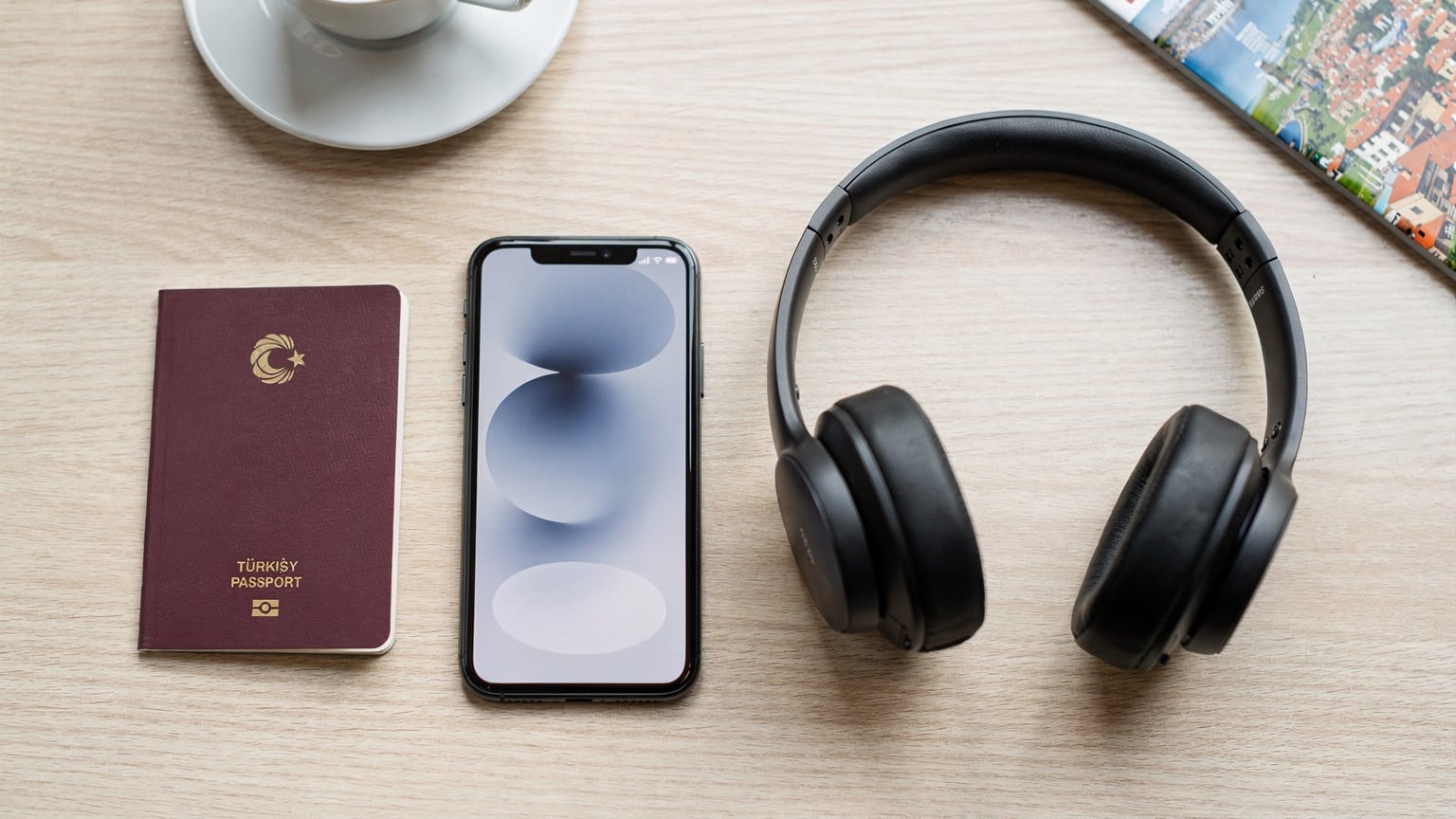 Bir seyahat blog yazarının pasaportunu, akıllı telefonunu ve kulaklığını gösteren bir düz çekim (flat-lay). Telefon ekranında bir eSIM sağlayıcısının uygulaması açık.
