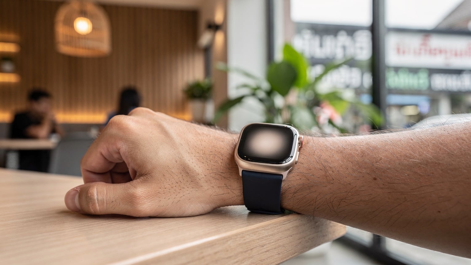 Nahaufnahme der Apple Watch Ultra 2 am Handgelenk einer Person, die in einem Café in Bangkok-Thonglor sitzt und eine Bestätigung auf dem Bildschirm sieht.