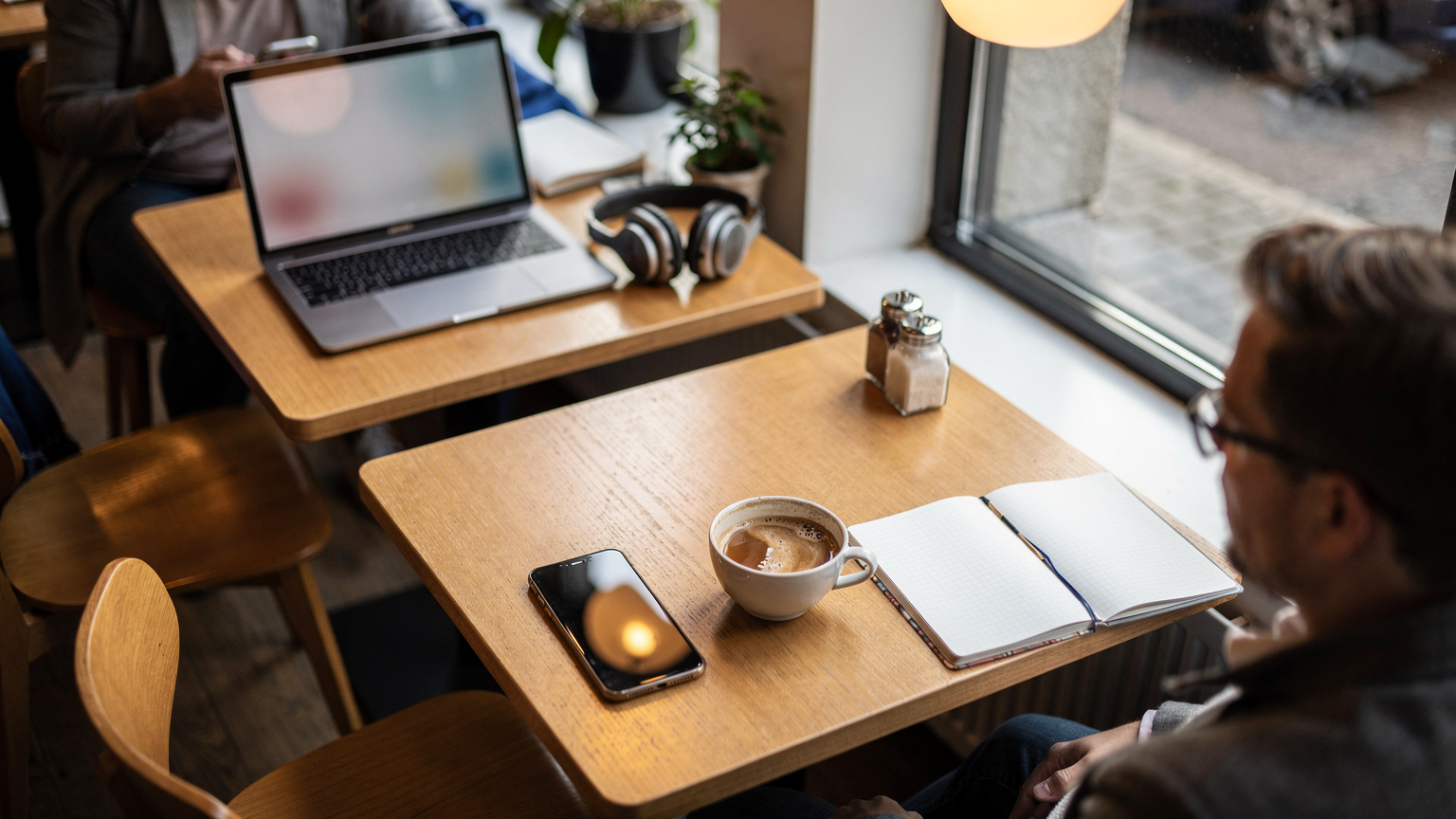 En travel kafe i Oslo sentrum, med fokus på en rekke mobiltelefoner og bærbare datamaskiner på bordene, og mennesker som jobber eller chatter i bakgrunnen. Atmosfæren er moderne og tilkoblet.