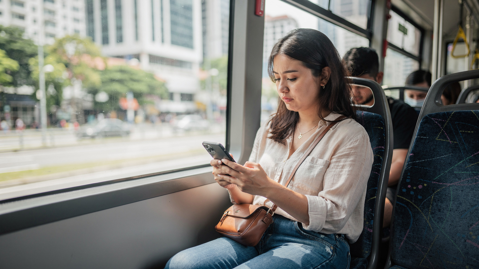 Seorang pengembara sedang menaiki bas SBS Transit di kawasan bandar Singapura, melihat telefon pintarnya yang memaparkan peta, mungkin untuk mencari Wi-Fi percuma.