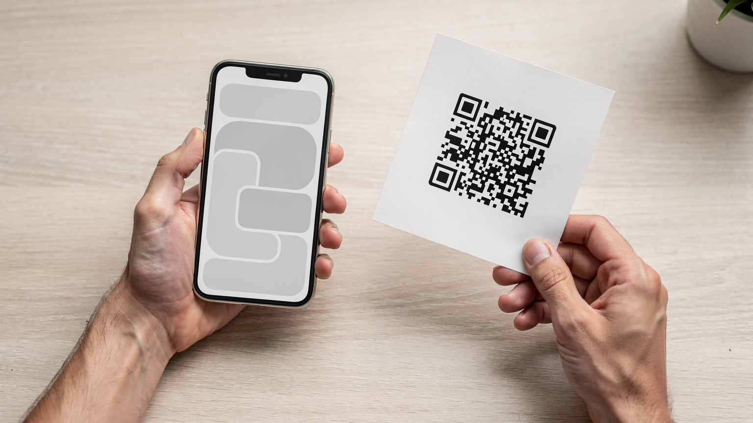 一雙成年人的手握著一部iPhone,螢幕上顯示著eSIM的設置介面。另一隻手拿著列印出來的QR碼準備掃描。背景是簡潔的桌面,暗示著在家中輕鬆設置eSIM的場景。