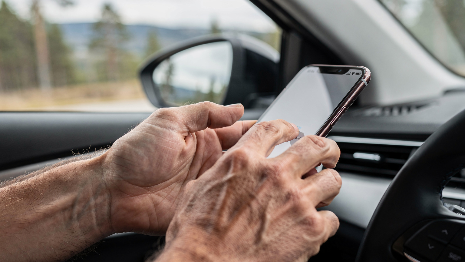 Close-up van handen die een smartphone vasthouden, waarbij de duim over het scherm veegt tijdens het instellen van een eSIM, met een vage achtergrond van een modern auto-interieur en een uitgestrekt landschap door het raam.