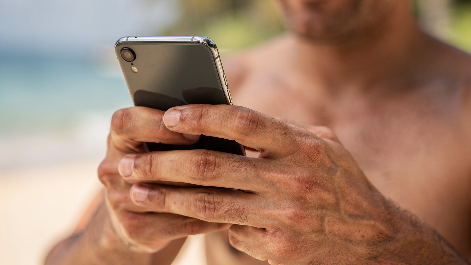 Un primer plano de manos humanas sosteniendo un smartphone, con el pulgar deslizando el dedo por la pantalla para configurar una eSIM. El fondo está desenfocado, mostrando colores tropicales de una playa.