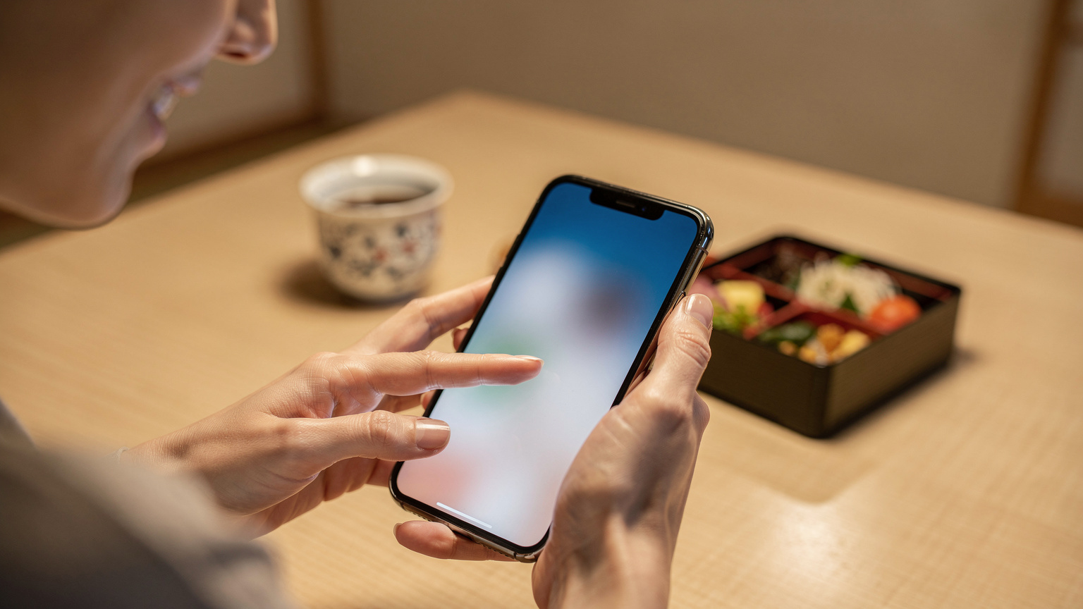 Tangan seorang ibu sedang mengatur pengaturan seluler di iPhone-nya, melabeli eSIM baru dengan nama 'Liburan Jepang' untuk memudahkan identifikasi.