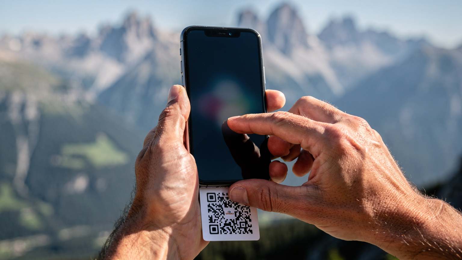 Un primo piano sulle mani di un viaggiatore che tiene il suo smartphone e sta scannerizzando un codice QR per attivare la sua eSIM, con lo sfondo sfocato di un paesaggio montano italiano.