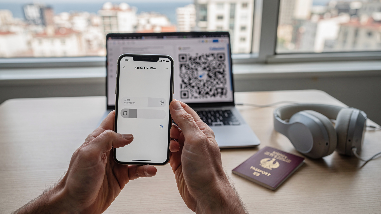 Bir seyahat blogu yazarının elinde akıllı telefonu, ekranda eSIM kurulum adımları açıkça görülüyor. Arka planda laptopunda Cellesim'den gelen QR kodu ve pasaportu masada duruyor. Şehir manzaralı bir pencere kenarında.
