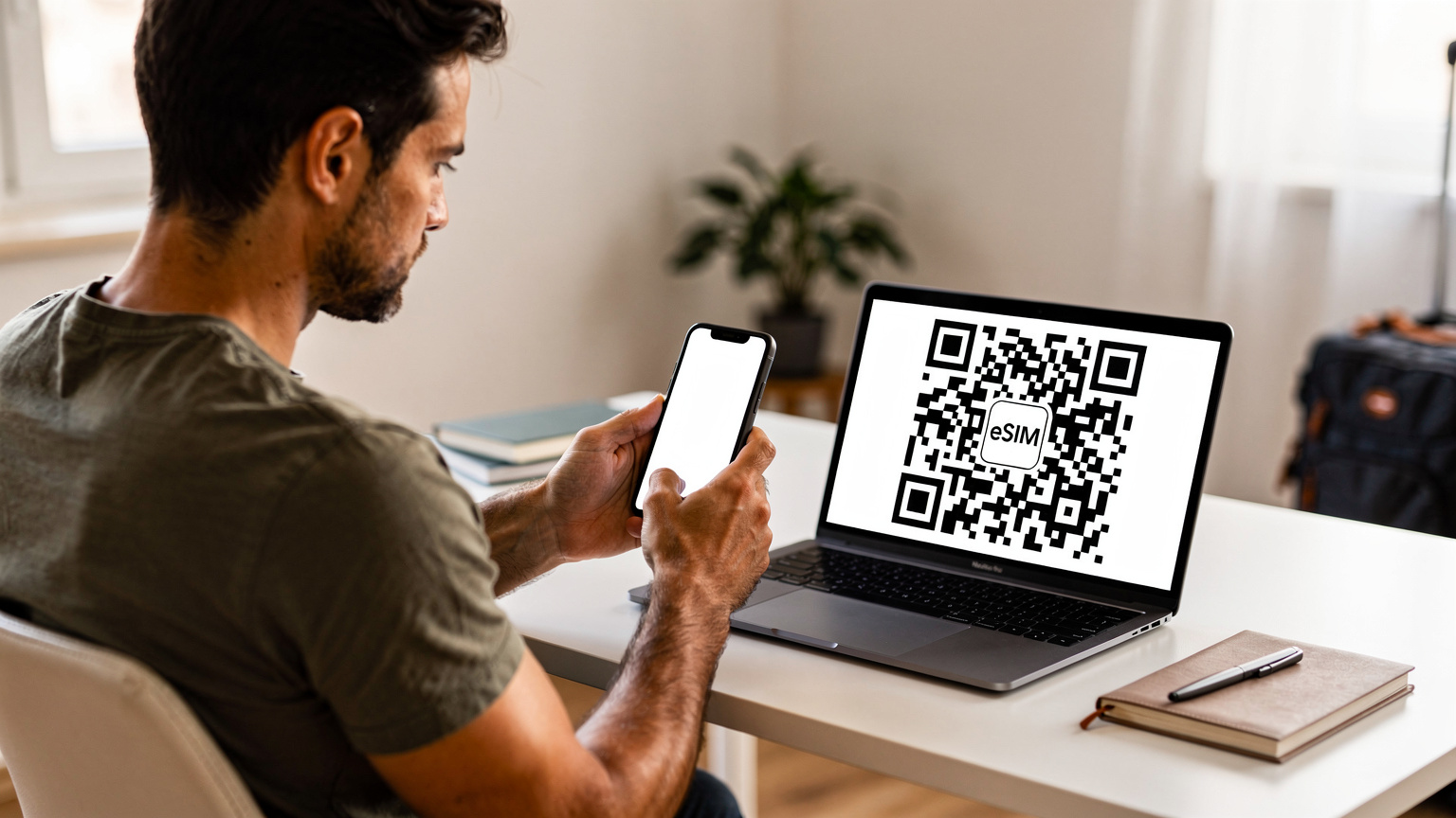 Un călător își verifică telefonul, având un cod QR pentru eSIM afișat pe ecranul unui laptop, într-un birou modern, pregătindu-se pentru călătorie.