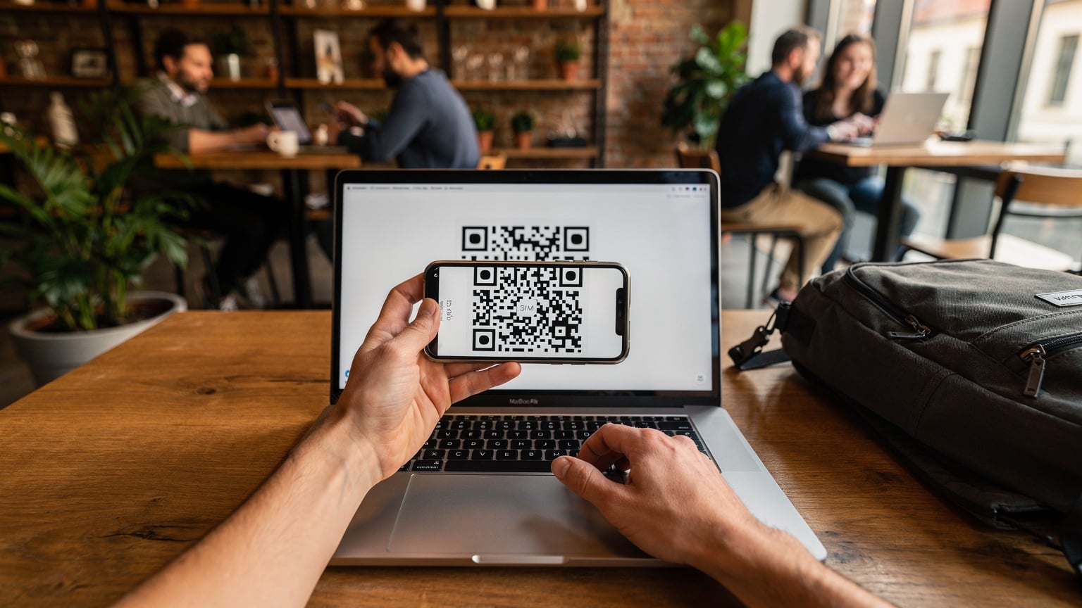Un călător își activează un eSIM pe telefonul mobil, scanând un cod QR de pe un laptop într-o cafenea aglomerată din Budapesta.