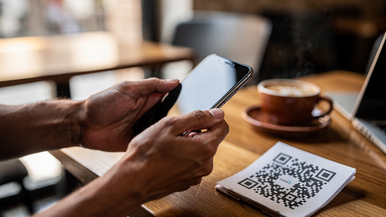 Unas manos sosteniendo un smartphone, mostrando el proceso de escaneo de un código QR para activar una eSIM, con un fondo ligeramente desenfocado de una cafetería moderna en Sevilla.