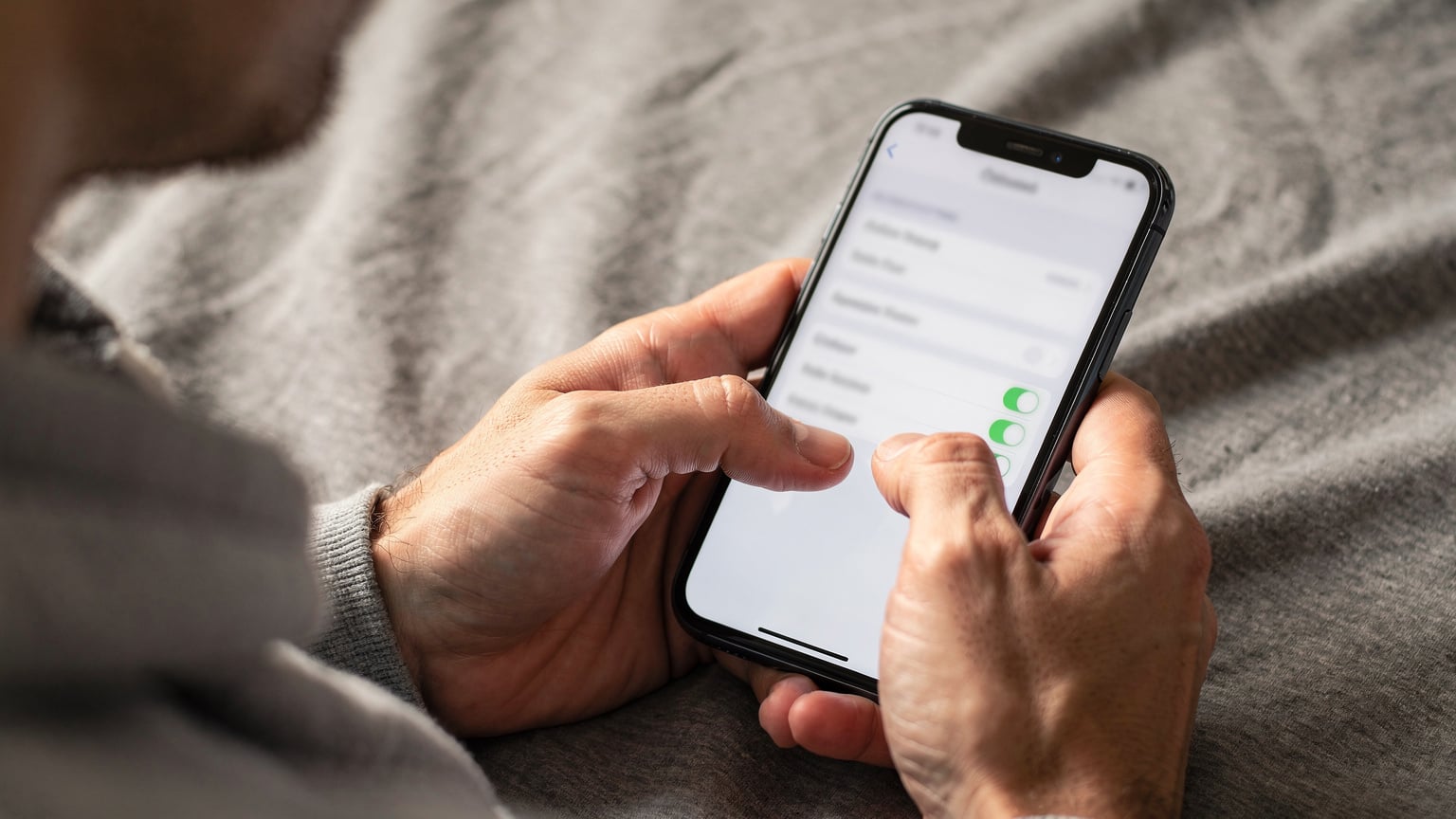 Close-up of human hands navigating iPhone cellular settings, showing the gesture of switching between data plans.