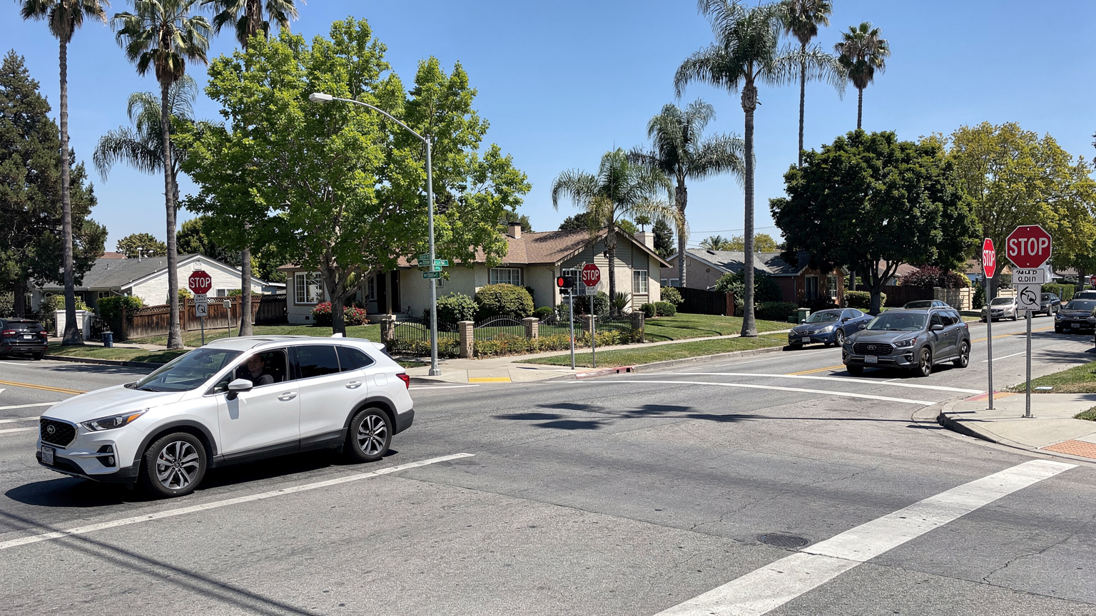 美国加州一个典型的四向停车路口,几辆不同类型的汽车,包括一辆SUV和一辆轿车,在标志牌前依次停车等待,阳光透过稀疏的树叶洒在路面上。