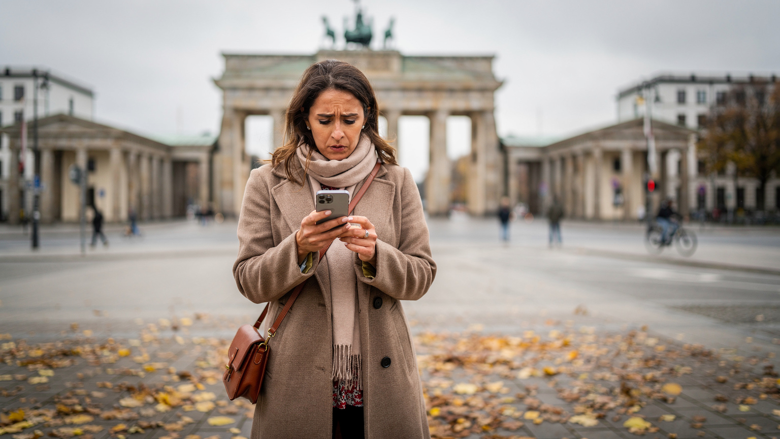 Een reiziger die bij de Brandenburger Tor in Berlijn staat, kijkt met een blik van verwarring naar haar smartphone, terwijl ze moeite heeft met het verkrijgen van internettoegang.