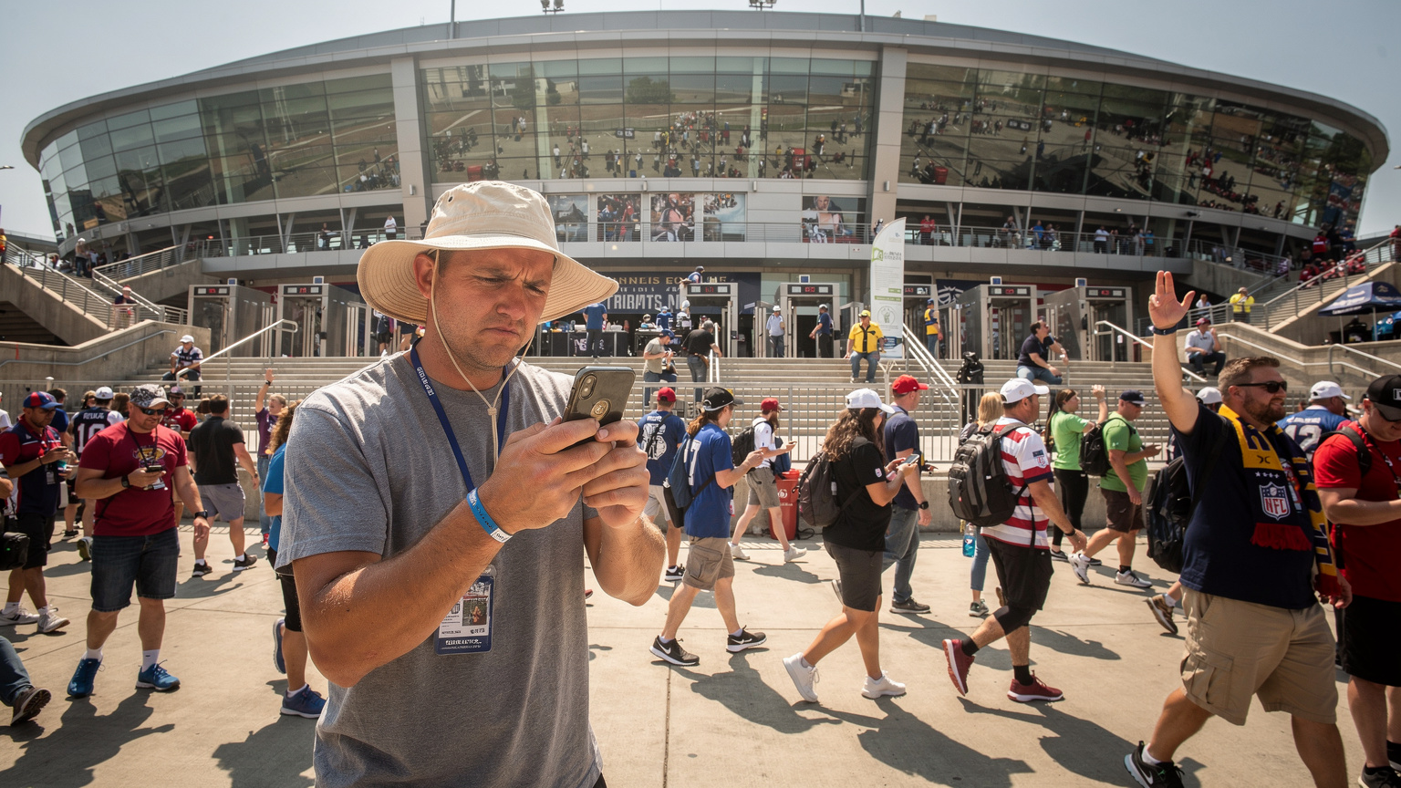 Um torcedor, usando um chapéu de sol, tenta usar o celular com sinal fraco no meio de uma multidão animada em frente a um estádio de futebol nos EUA antes de um jogo da Copa América.