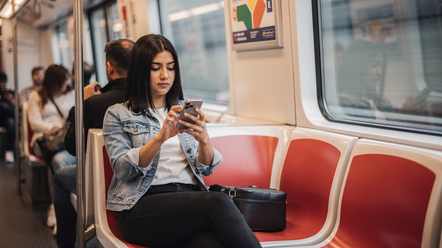 Madrid metrosunda, oturarak telefonunda eSIM ayarlarını inceleyen bir yolcu.