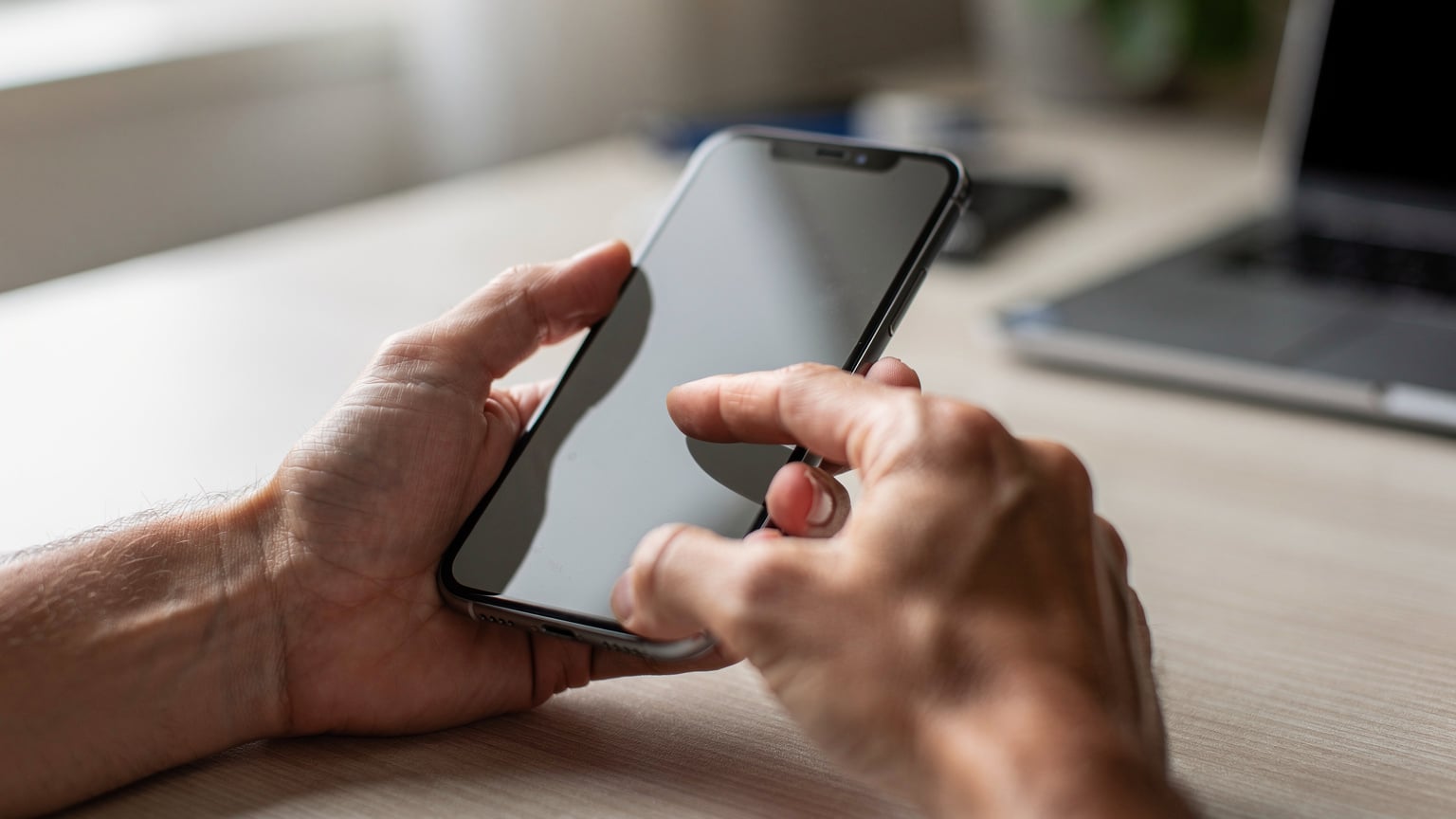 Close-up of human hands holding a smartphone, with a finger delicately tapping the screen to confirm an eSIM installation.